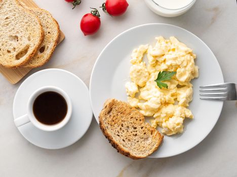 Breakfast with pan-fried scrambled eggs, cup of coffee, tomatoes on a white stone background. Omelette, top view