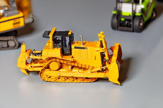 Toy model of a yellow construction bulldozer on a light gray background, selective focus, copy space.