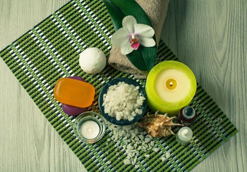 Spa setting with orchid flower, bowl with sea salt, seashell, bottles with aromatic oil, soap, candles and towel on bamboo napkin
