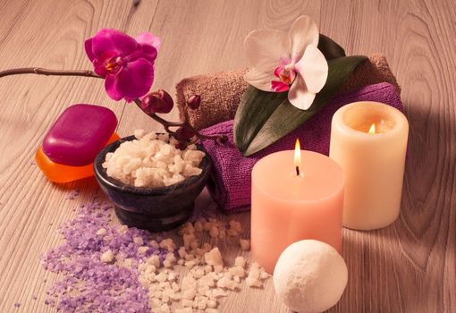 Spa setting with orchid flowers, bowl with sea salt, candles, soap and towels on wooden board
