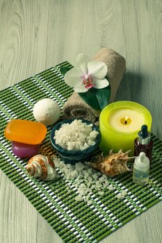 Spa accessories with orchid flower, bowl with sea salt, seashells, bottles with aromatic oil, soap, candles and towel on bamboo napkin
