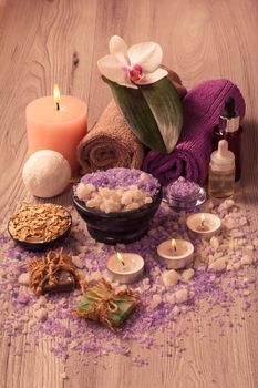 Spa accessories with orchid flower, bowl with sea salt, bottles with aromatic oil, soap, scrub, candles and towels on wooden board