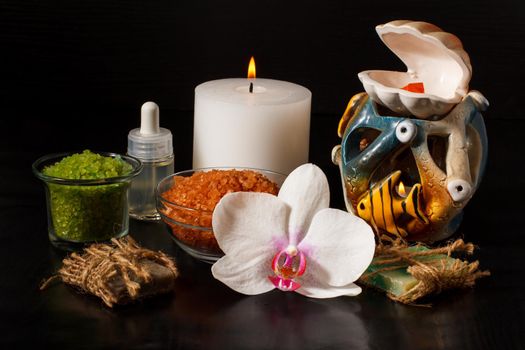 Spa products with orchid flower, handmade soap, bowls with sea salt, bottle with aromatic oil, candles on black background