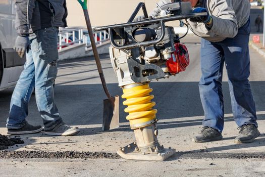 Road workers use vibratory rammer to asphalt a small section of road on a bright sunny day, selective focus.