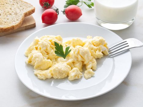 The white plate with pan-fried scrambled eggs on a white light background with tomatoes. Omelette, side view