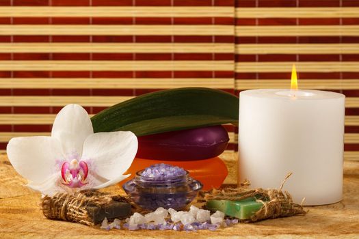 Spa products with orchid flower, bowl with sea salt, handmade soap, candle on wooden board