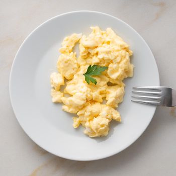 white plate with pan-fried scrambled eggs on a white light background with tomatoes. Omelette, top view