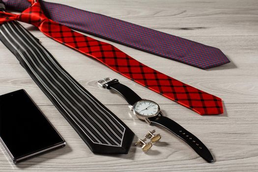 Color silk neckties, watch with a leather strap, cufflinks, sell phone on a gray wooden background