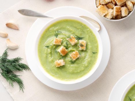 large white bowl with vegetable green cream soup of broccoli, zucchini, green peas on a white background, top view