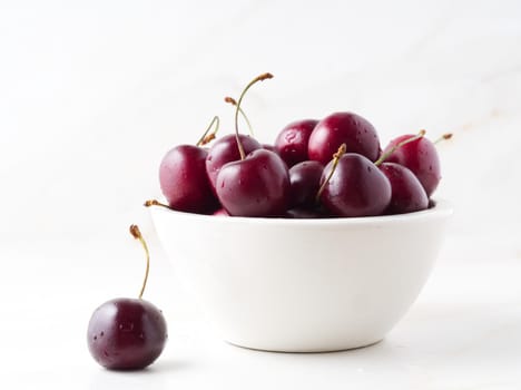 The red dark sweet cherries in white bowl on stone white table, side view.