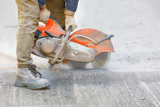 A worker repairs a section of road, cuts worn asphalt in a cloud of dust with a portable asphalt cutter and a diamond cutting disc, copy space, close-up.