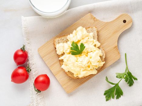 Sandwich with pan-fried scrambled eggs on a wooden cutting board, top view.