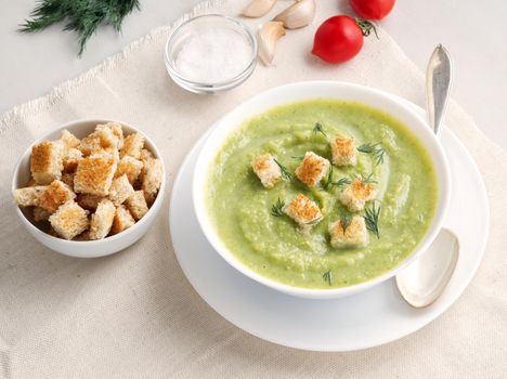 large white bowl with vegetable green cream soup of broccoli, zucchini, green peas on a white background, side view