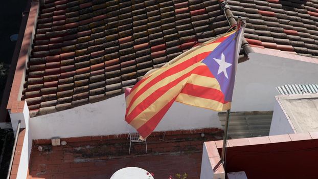 Catalan flag flies in the wind on sunny day at the background of a tiled roof