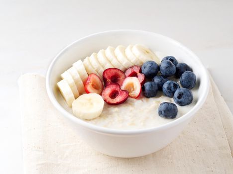 Large bowl of tasty and healthy oatmeal with a fruits and berry for Breakfast, morning meal. Side view, white marble table