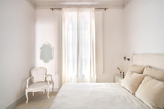 Bright bedroom interior, cozy bed with beige linen, dry flowers on a bedside table. Daylight shines through a window with a curtain