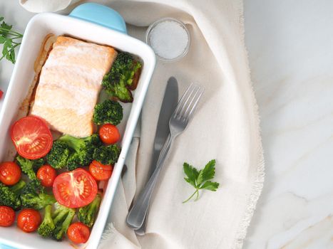 Fish salmon baked in oven with vegetables - broccoli, tomatoes. Healthy diet food, white marble backdrop, top view, close-up