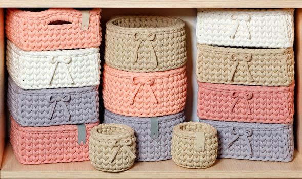 Multi-colored wicker textile baskets for storing women's jewelry on a wooden shelf, close-up.