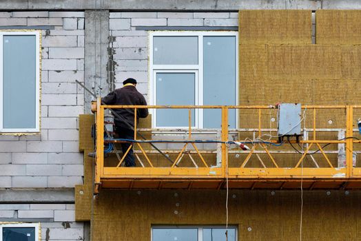 The builder insulates the facade of the house with mineral wool using a construction cradle.