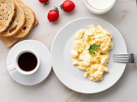 Breakfast with pan-fried scrambled eggs, cup of coffee, tomatoes on a white stone background. Omelette, top view