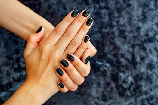 Woman's hands with beautiful manicure beautiful black with gel glitter on a velvet dark blue background, copy space.