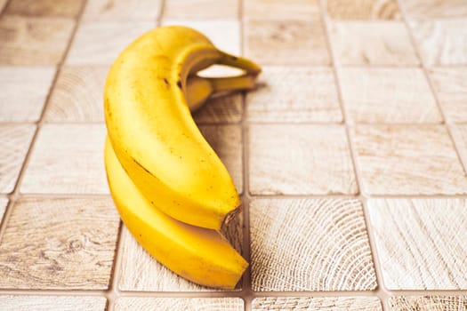 a long curved fruit which grows in clusters and has soft pulpy flesh and yellow skin when ripe.Two ripe bananas on a checkered wooden surface.