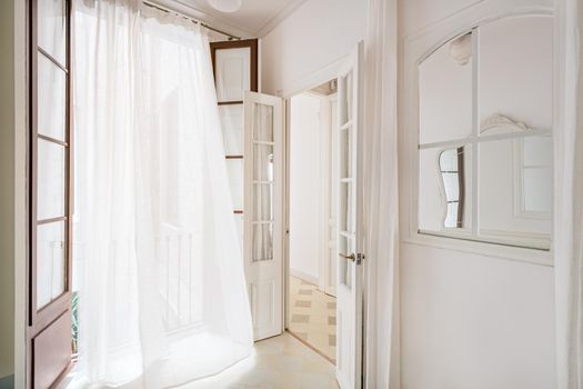 White waving curtain in empty room of refurbished apartment in Barcelona. Classic style interior with window and mirror