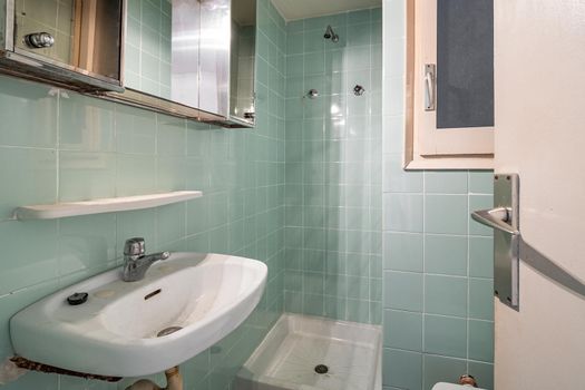 Old and dirty bathroom with faucet, shower zone and blue tiles in an old house of Barcelona