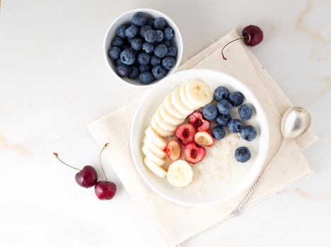 Large bowl of tasty and healthy oatmeal with a fruits and berry for Breakfast, morning meal. Top view, white marble table