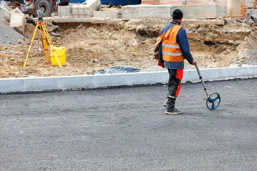 A working engineer measures road distances with a measuring wheel and determines the amount of asphalt needed to be poured on a new section of road.