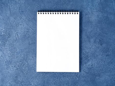 The open notepad with clean white page on a aged dark blue stone table, top view