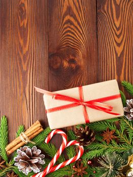 Christmas and Happy New Year dark brown background. Gift Christmas box, fir branches, wooden table, top view, copy space, vertical.