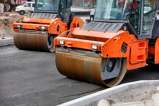 The metal cylinders of the large vibratory rollers forcefully compact the fresh asphalt of the road surface. Copy space.