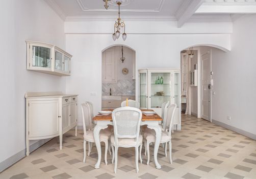 Dining table in a center of living room decorated in retro style. Tile floor and vintage chandeliers in refurbished apartment in Barcelona. Beautiful bright interior.