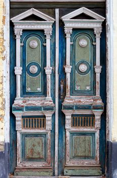 Old high wooden entrance doors in white, blue and green with carved elements frame the entrance of the old house in a carved symmetrical pattern.