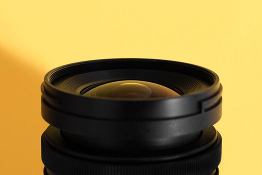 Close-up of an wide angle camera lens with glass reflections on yellow background. Selective focus.