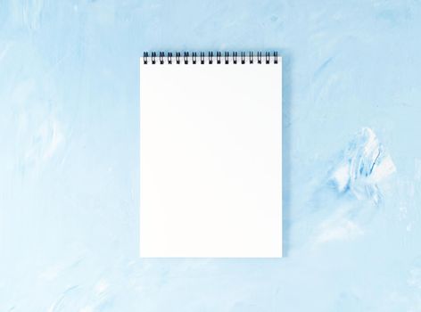 Top view of modern bright blue office desktop with a notepad. Mock up, empty space