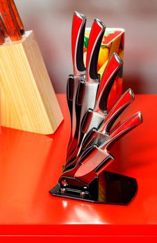 A set of beautiful stainless steel metal kitchen knives in a black elegant case on a red background.