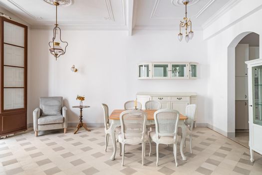 Dining table in a center of living room decorated in retro style. Tile floor and vintage chandeliers in refurbished apartment in Barcelona. Beautiful bright interior.