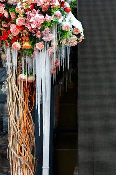 Snow-covered flowers on the terrace with long hanging icicles. Vertical image, copy space.