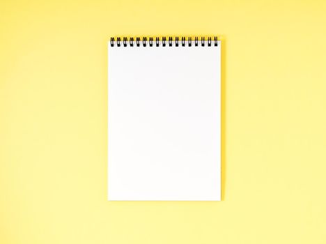 Blank notepad white page on yellow desk, a color background. Top view, empty space for text.