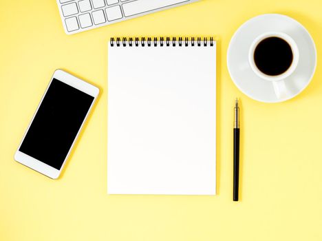 Top view of yellow office desktop with a notepad, computer keyboard, smartphone. Mock up, empty space