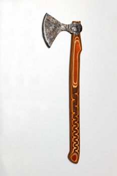 A battle ax of an antique Ukrainian warrior with an old forged blade and a wooden handle made of multilayer wood with a printed pattern, on a gray silver background. Copy space, vertical image.