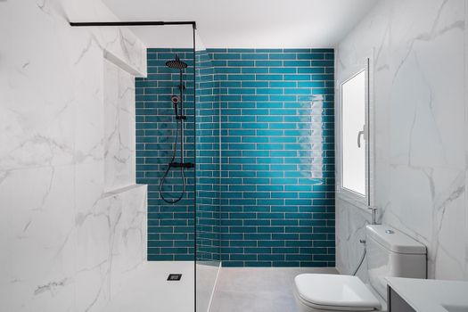 Decorated with dark aquamarine and white colors. Modern tiled bathroom with shower zone, new sink and toilets