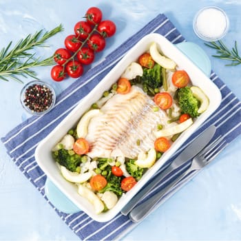 Fish cod baked in blue oven with vegetables - broccoli, tomatoes. Healthy and diet food. Blue stone background, top view.