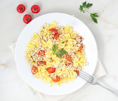 farfalle pasta with tomatoes, chiken meat, parsley on white stone background, low-calorie diet, the top view