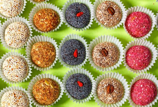 Collection of handmade energy balls with various seed fillings in paper baskets, healthy dessert and appetizer on a bright light green background.