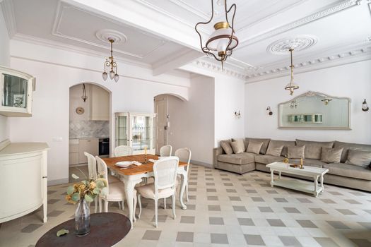 Classic room with dining table, served for two persons, sofa, tile floor, light walls and vintage chandeliers.