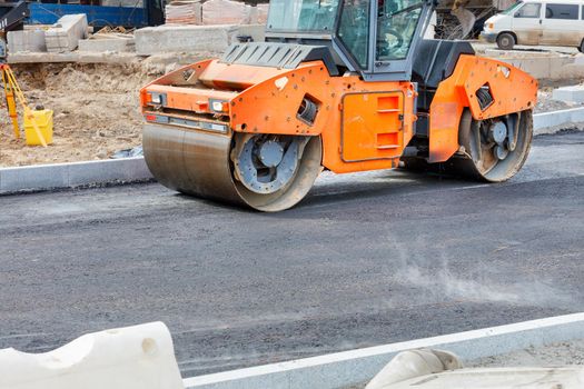 Large vibratory roller compact fresh asphalt on the road surface of a new construction site. Copy space.