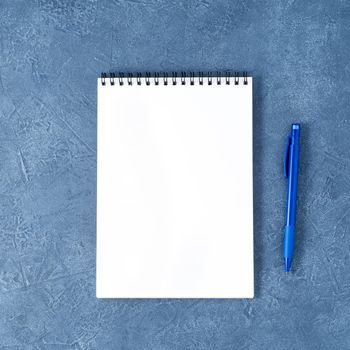 The open notepad with clean white page on a aged dark blue stone table, top view